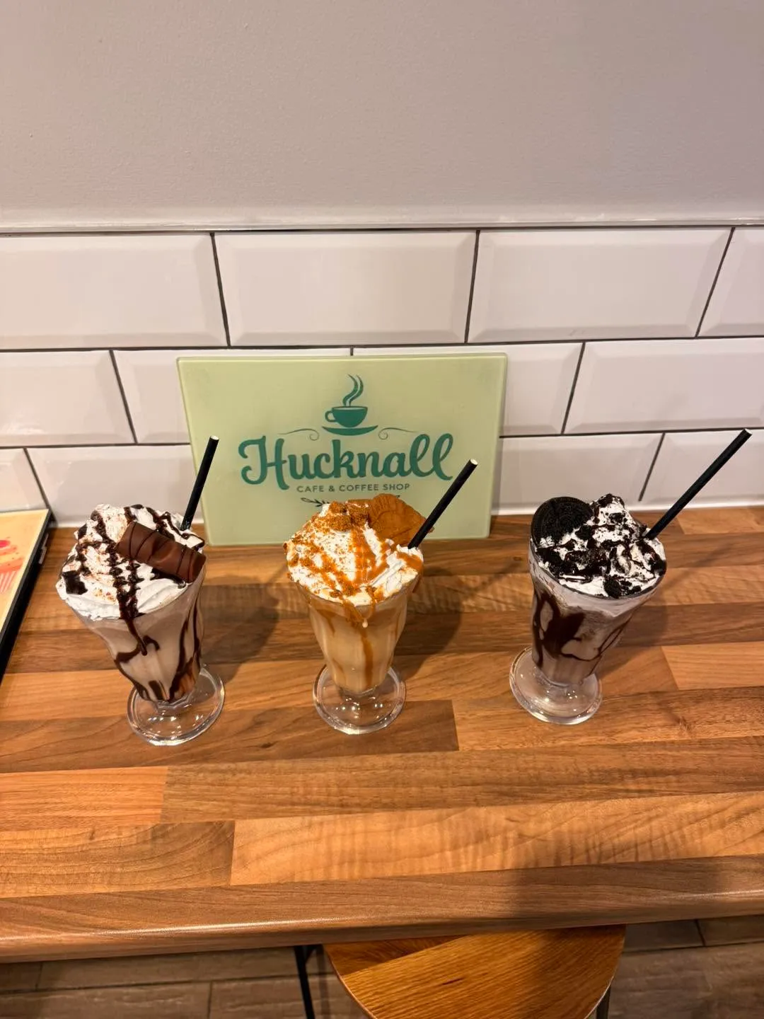 Kinder Bueno, Biscoff and Oreo milkshakes topped with cream in front of the Hucknall Cafe sign