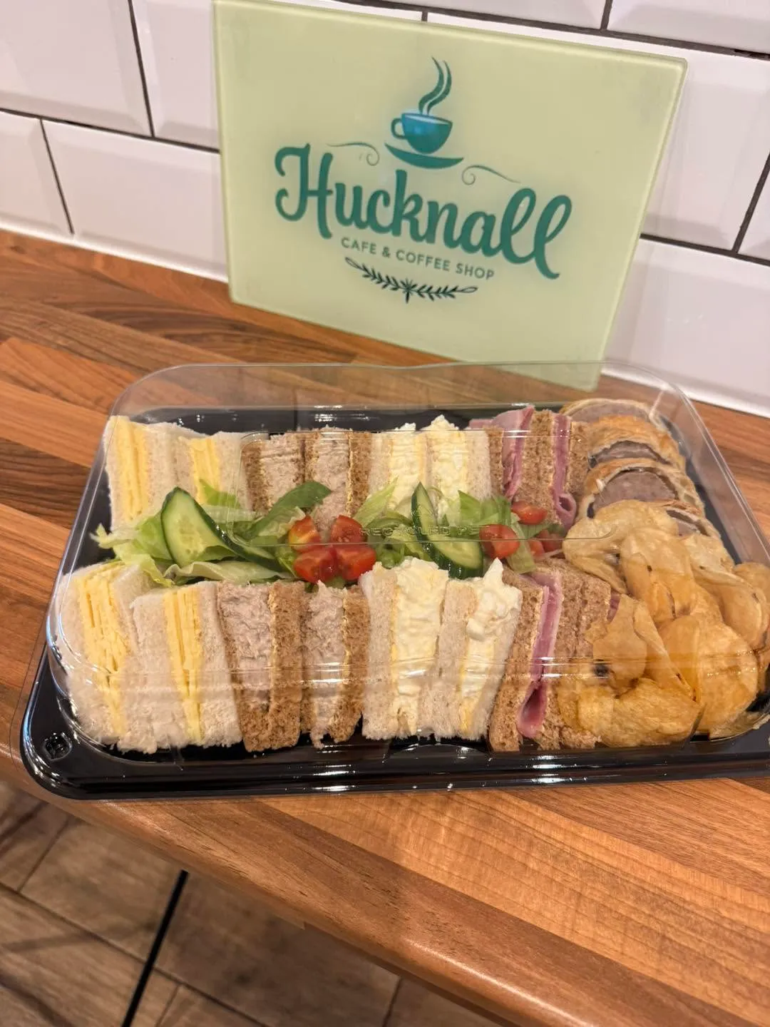 Takeaway afternoon tea box of sandwiches, salad and crisps in front of the Hucknall Cafe sign